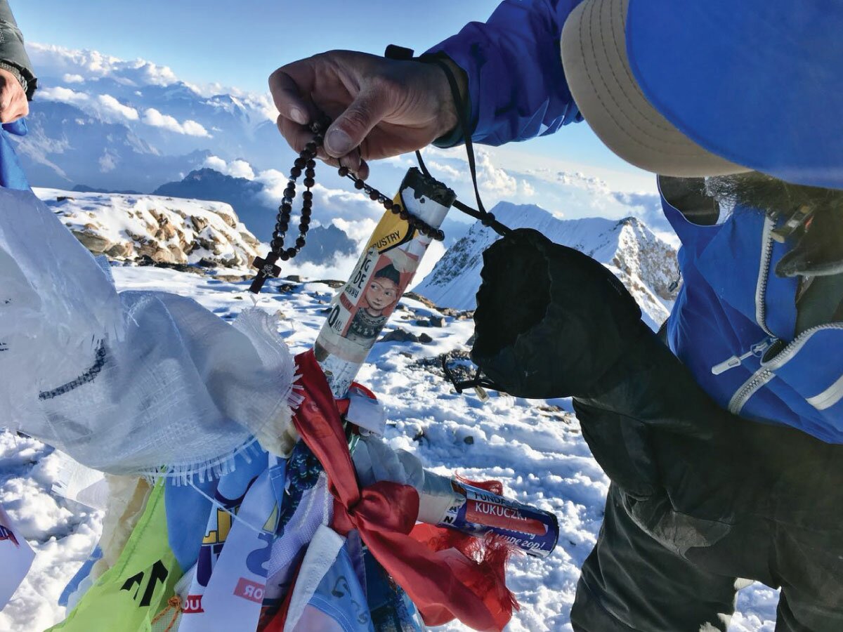 Ulises Corvalan poniendo un Rosario en la cruz de la cumbre